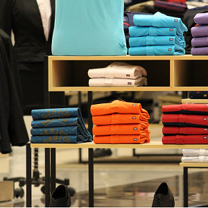 Neatly organized display of colorful folded shirts on a store shelf, showcasing retail clothing merchandising.