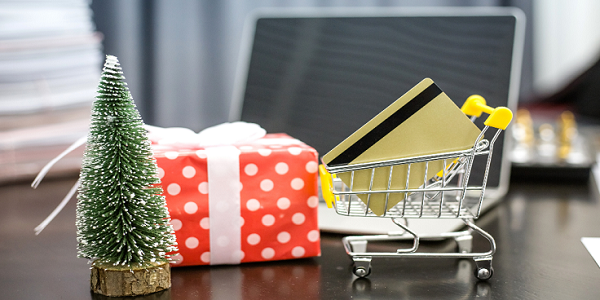 Holiday shopping concept with a miniature shopping cart and credit card on a desk, indicating online shopping.